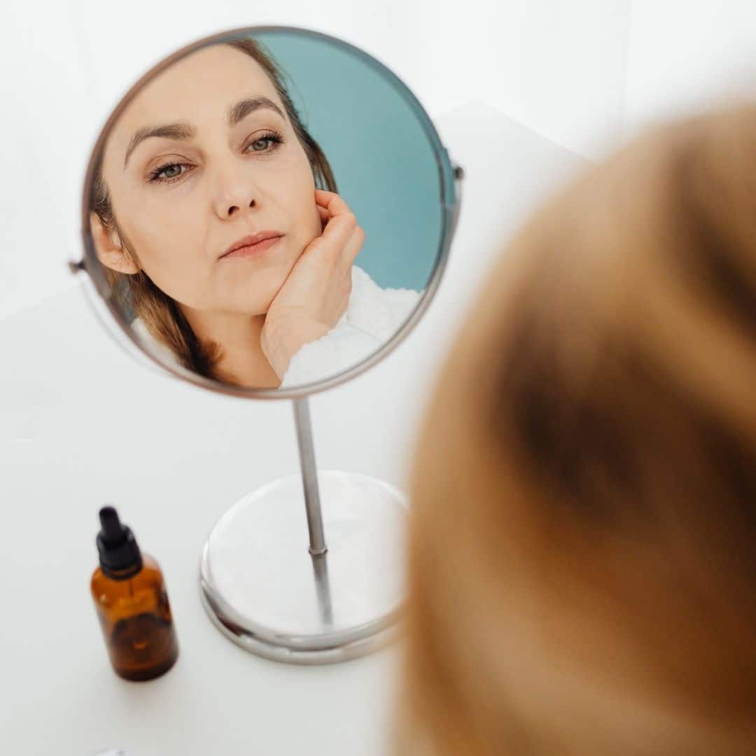a woman looking at herself in the mirror with serum nearby